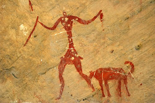 A man stands tall next to his dog in an early cave painting